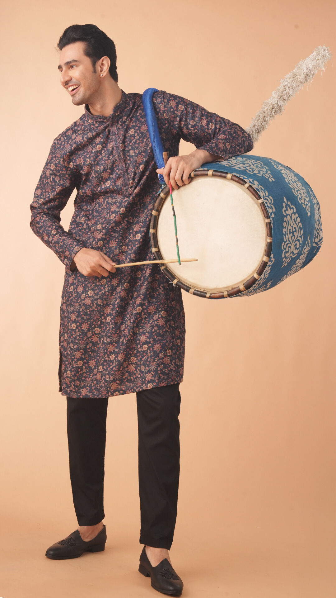 Man in a printed kurta with black pants playing a traditional dhol during Durga Puja celebration